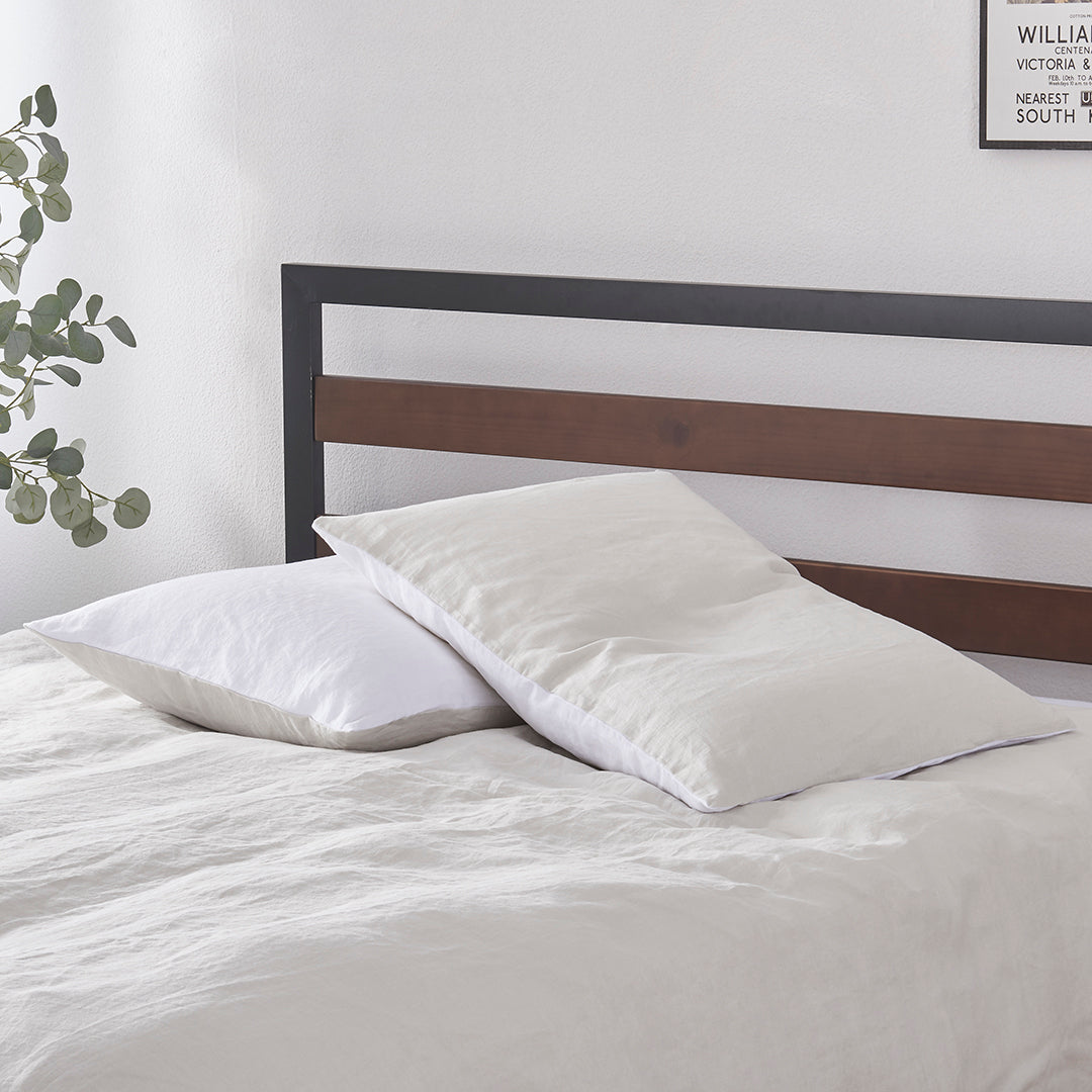 A pair of cool grey and white 100% linen two tone pillowcases stacked on a bed