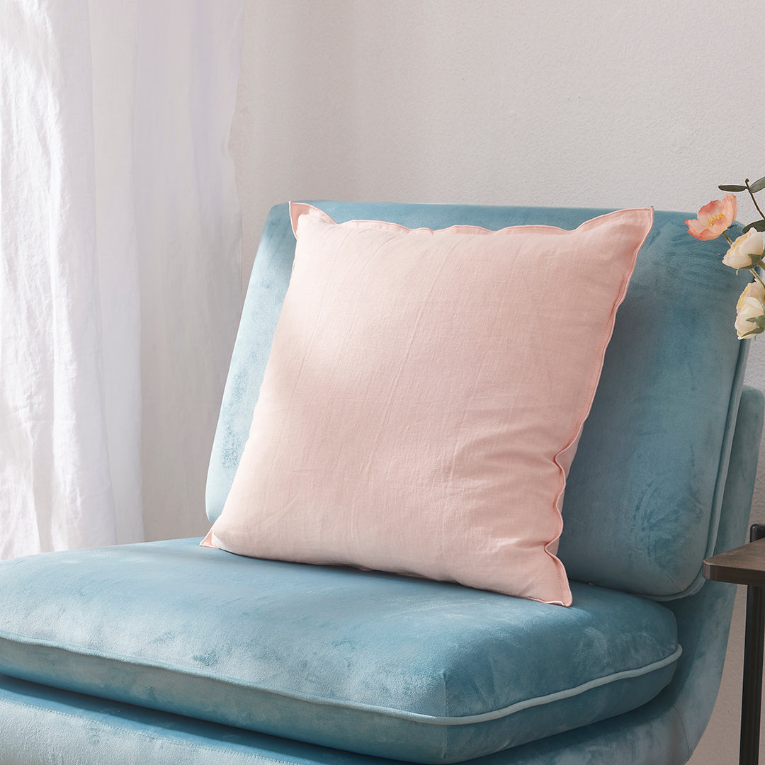 Side angle of a peach 100% linen edge embroidery cushion on an accent chair