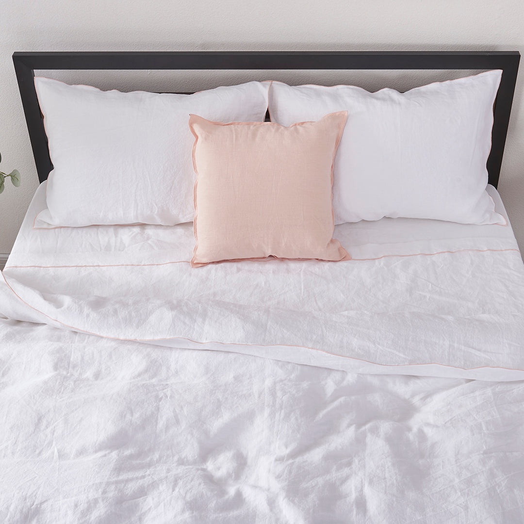 Top angle of a linen duvet cover with peach embroidered edges draped over a bed