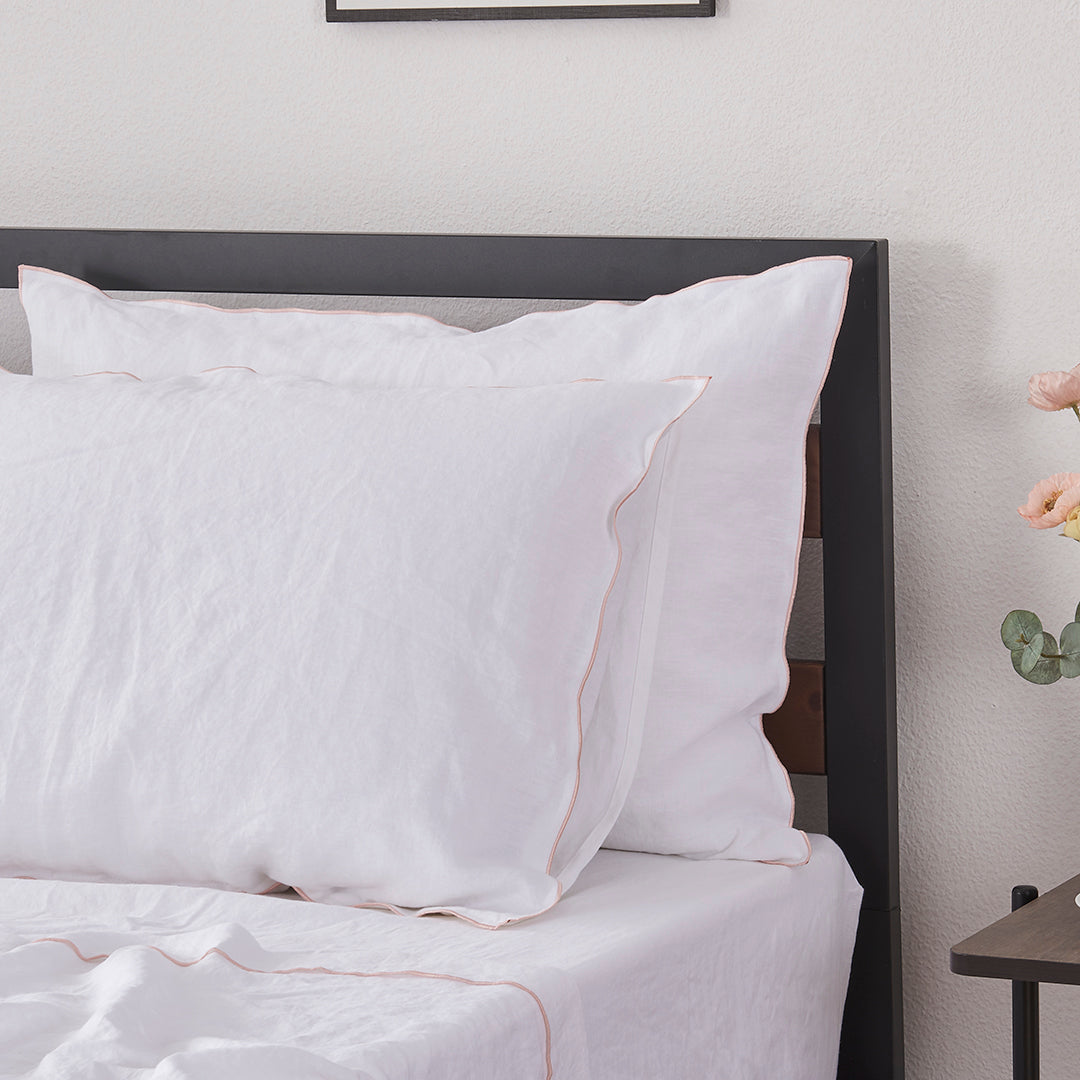 Close-up of a pair of stacked 100% linen pillowcases with edge embroidery in peach