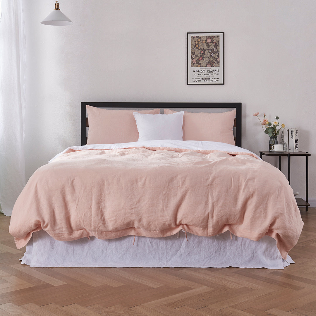 Bottom angle of 100% linen two tone duvet cover in peach and white draped over a bed