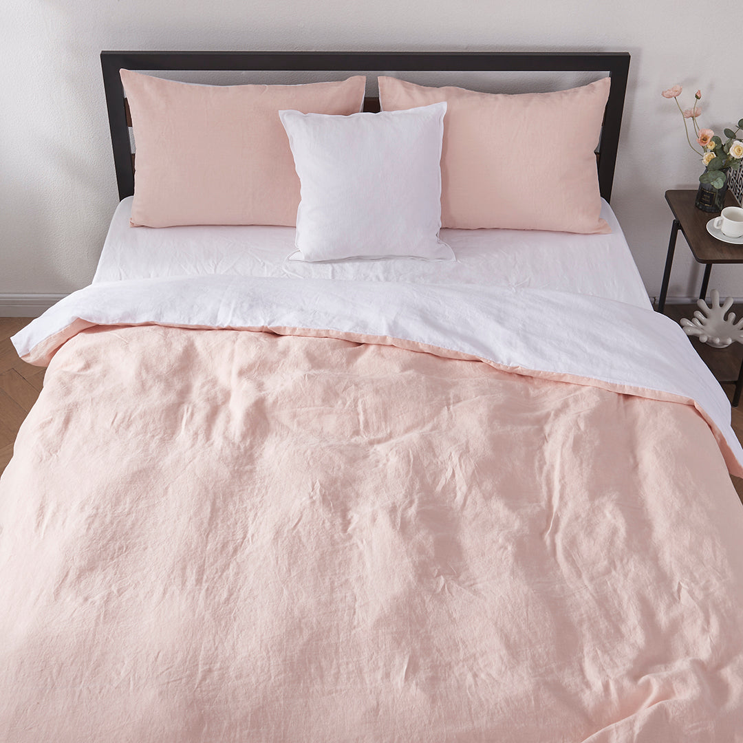 Top angle of 100% linen two tone duvet cover in peach and white draped over a bed