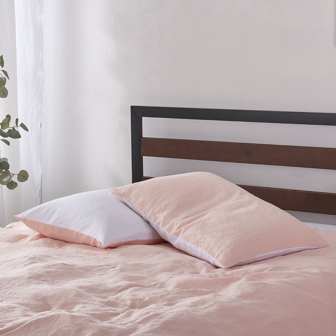 A pair of peach and white 100% linen two tone pillowcases stacked on a bed