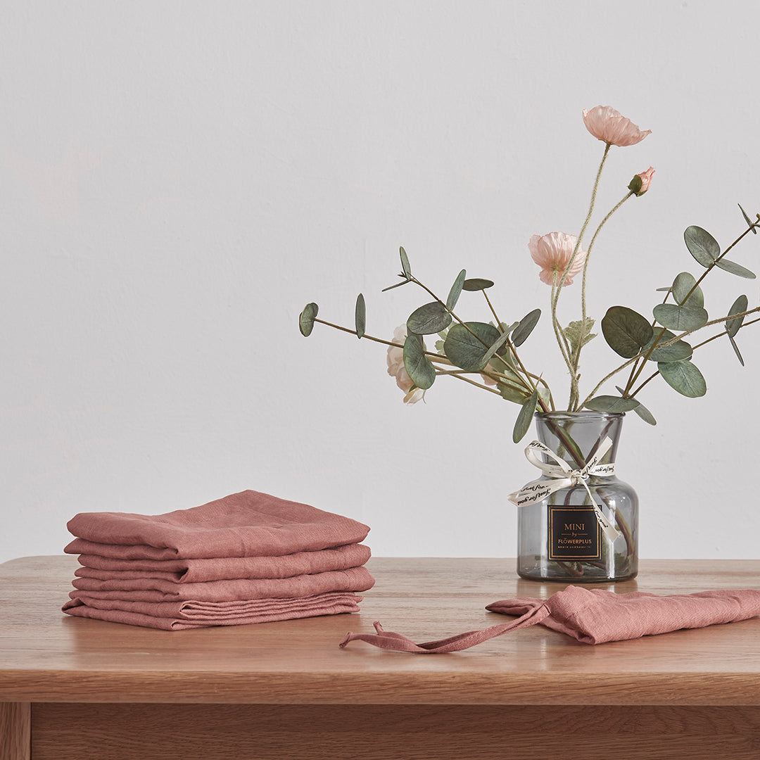 Rust red 100% linen placemats folded on a wooden dining table with flower vase