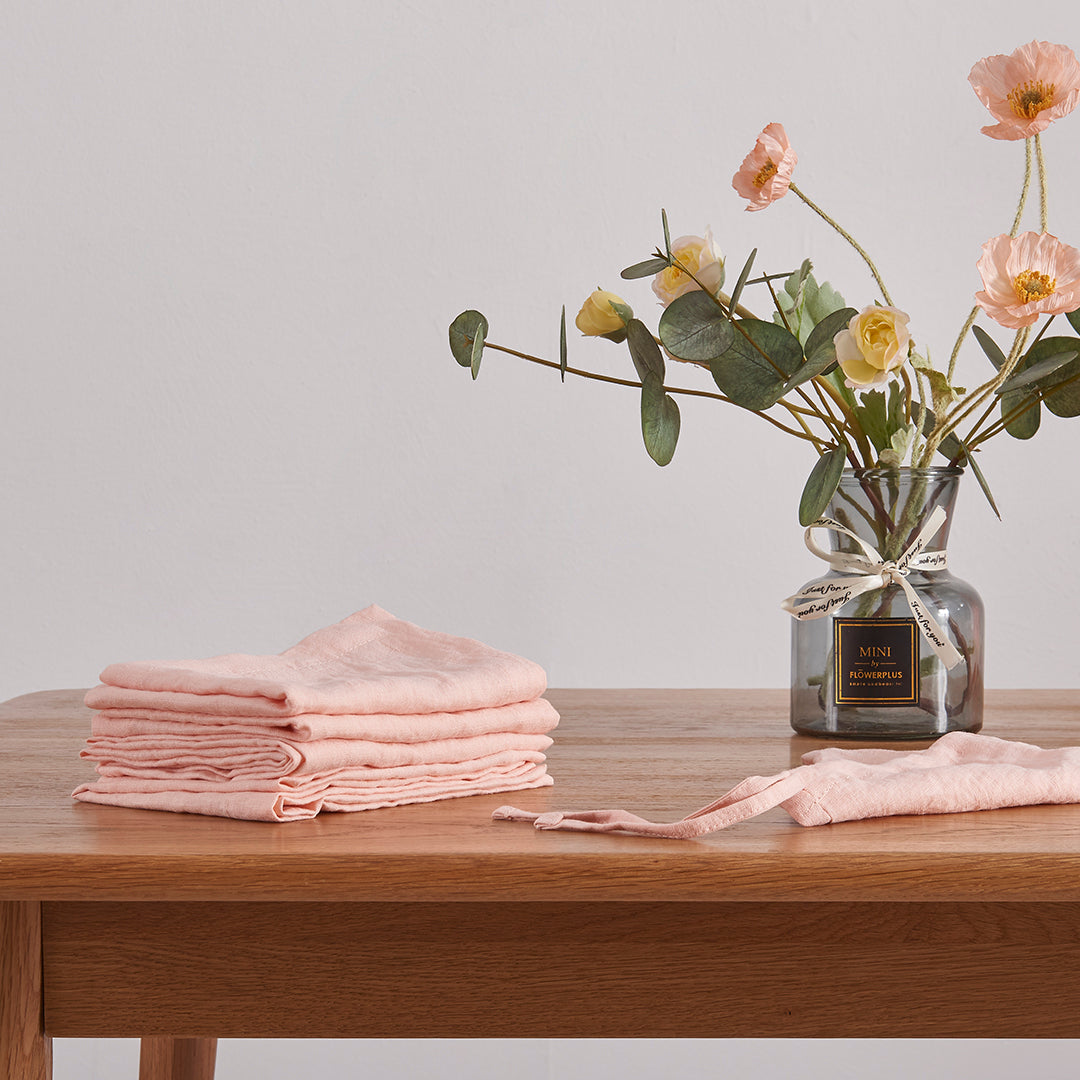 Peach 100% linen placemats folded on a wooden dining table with flower vase