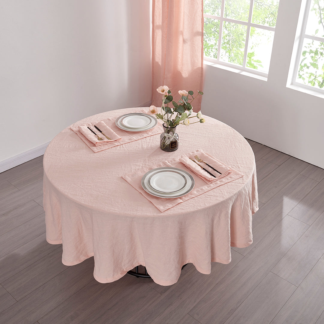 Top angle of 100% linen round tablecloth in peach draped over a round table set with plates and cutlery