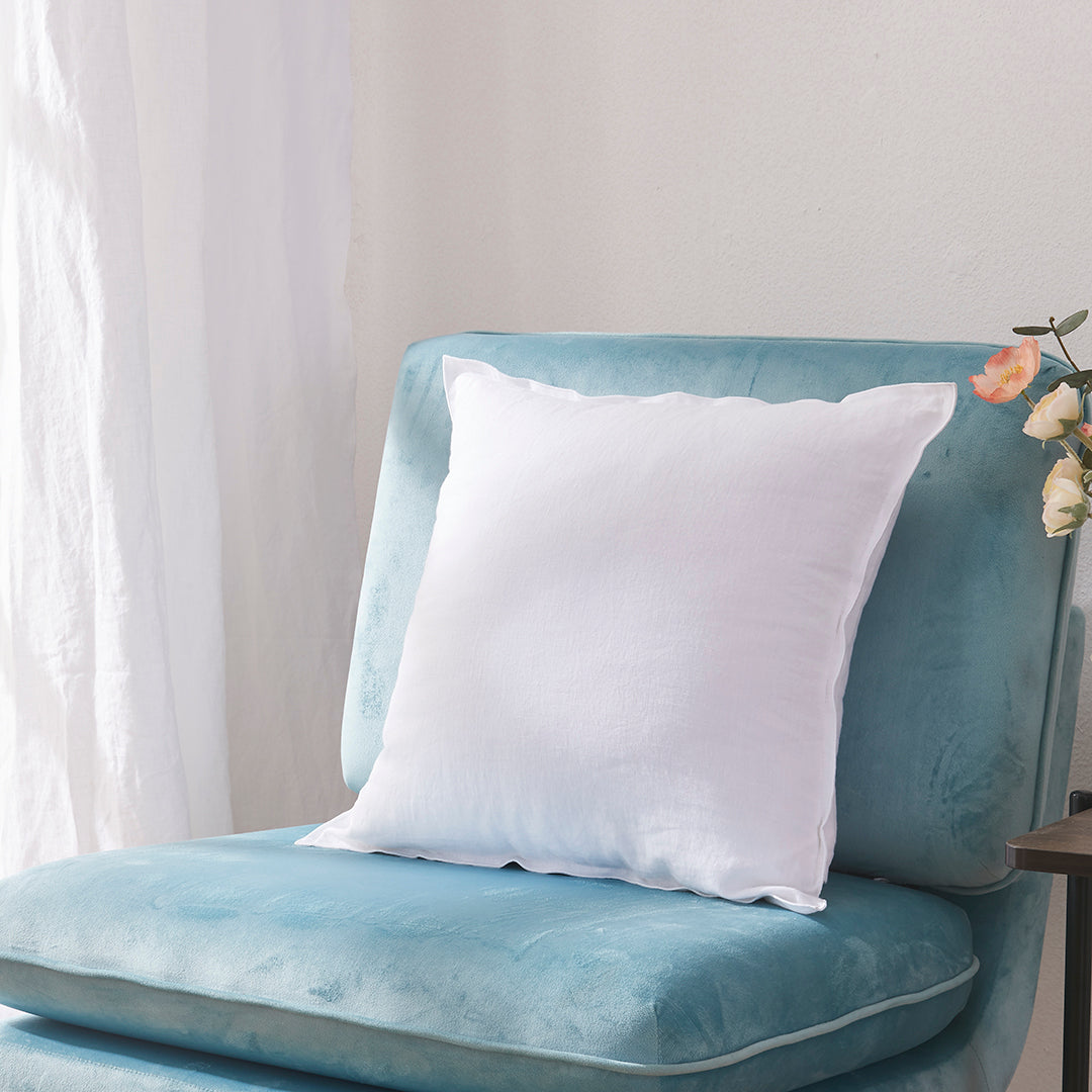 Side angle of a white 100% linen edge embroidery cushion on an accent chair
