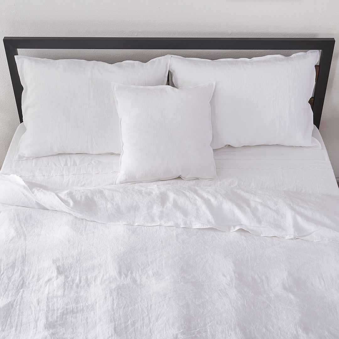 Top angle of a linen duvet cover with white embroidered edges draped over a bed