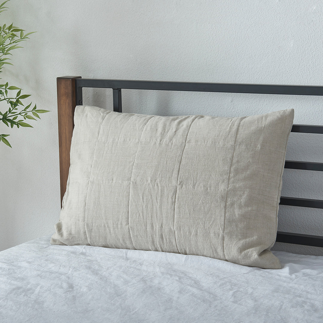 A natural 100% linen quilted pillowcase propped up against bed headboard