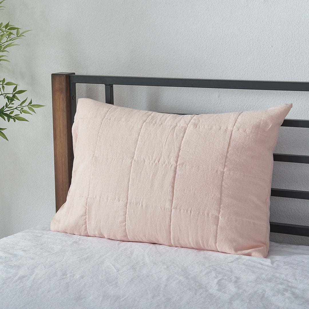 A peach 100% linen quilted pillowcase propped up against bed headboard