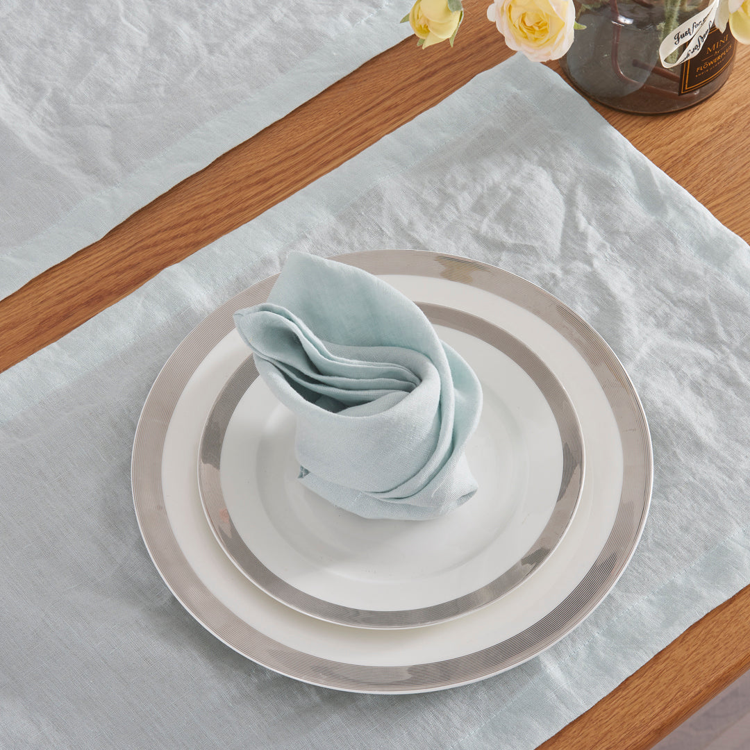 A folded pale blue linen table napkin on top of a white ceramic plate.