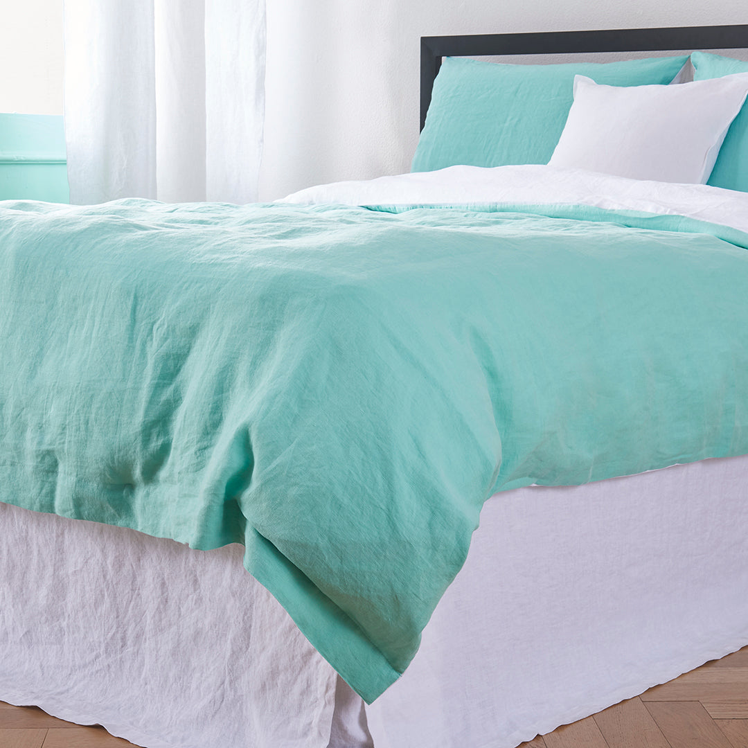 Corner bottom angle of 100% linen two tone duvet cover in aqua green and white draped over a bed