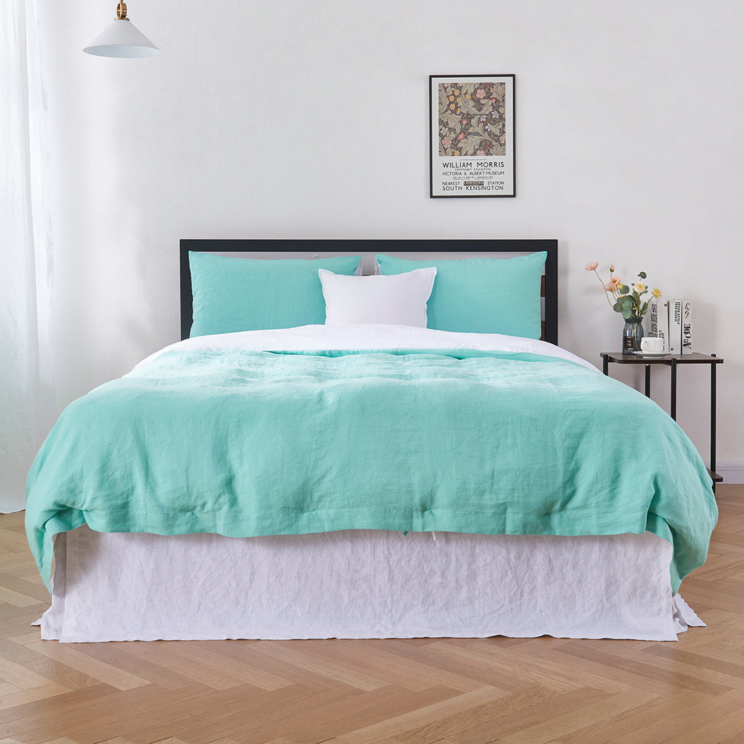 Bottom angle of 100% linen two tone duvet cover in aqua green and white draped over a bed