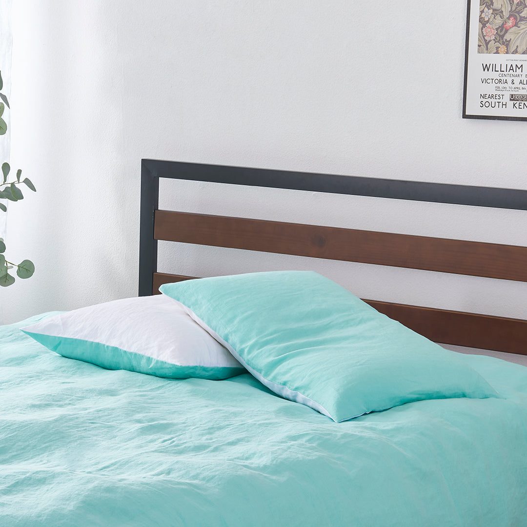 A pair of aqua green and white 100% linen two tone pillowcases stacked on a bed