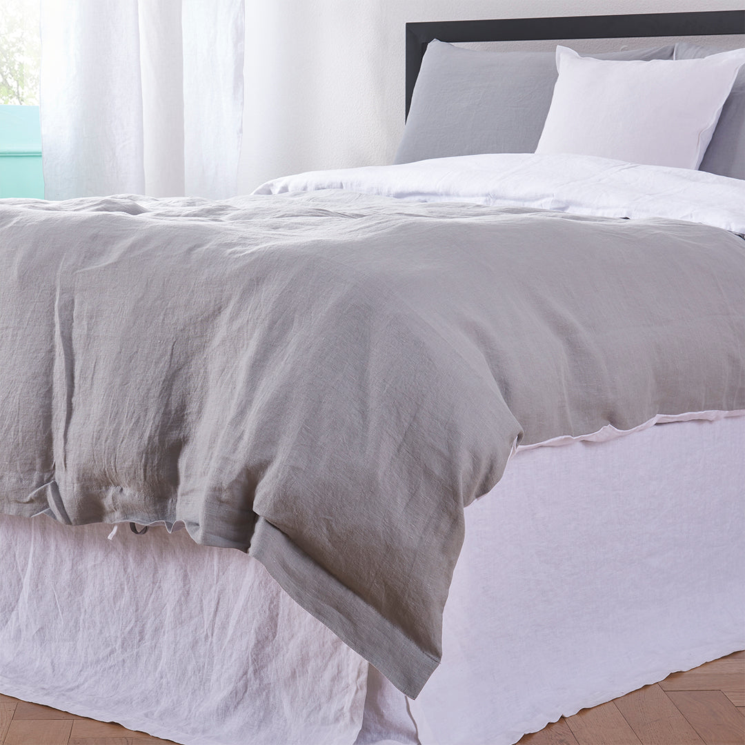 Corner bottom angle of 100% linen two tone duvet cover in alloy grey and white draped over a bed