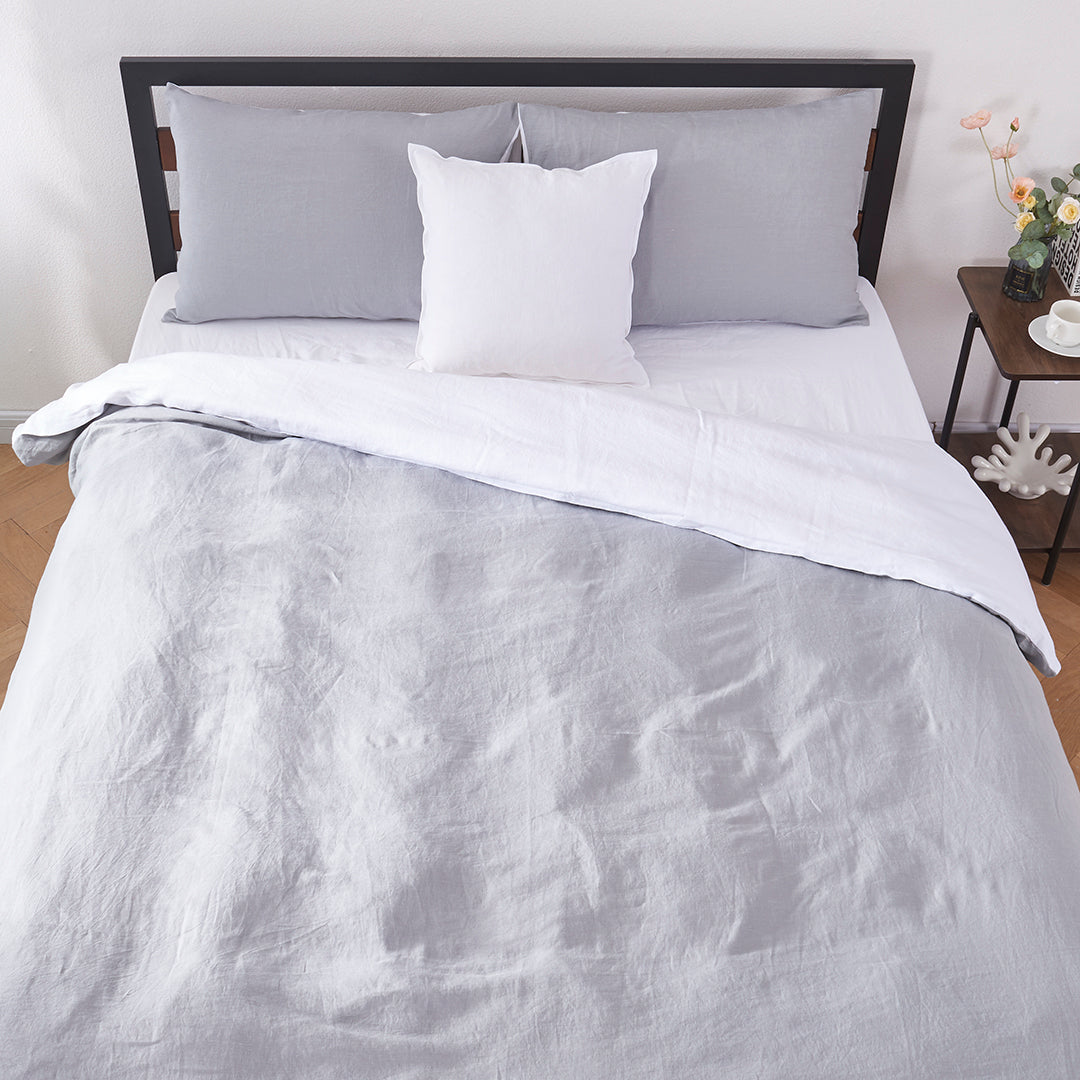 Top angle of 100% linen two tone duvet cover in alloy grey and white draped over a bed