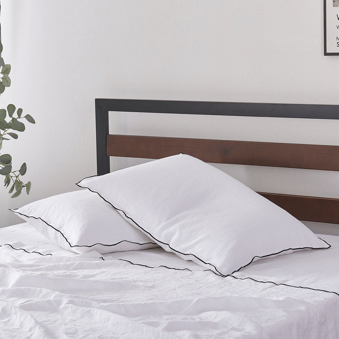 Pair of 100% Linen White Pillowcases with Black Embroidered Edge on Bed