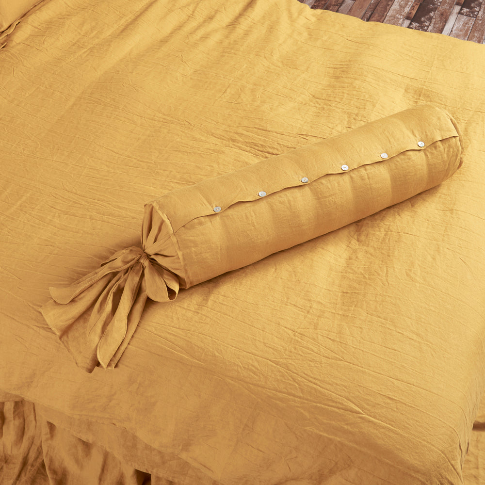 100% linen bow tie bolster with ruffles on a bed with shell buttons in mustard