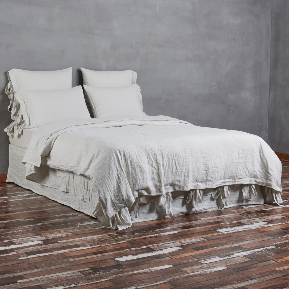 A side profile view of a bed with a cool grey 100% linen duvet cover with bow ties