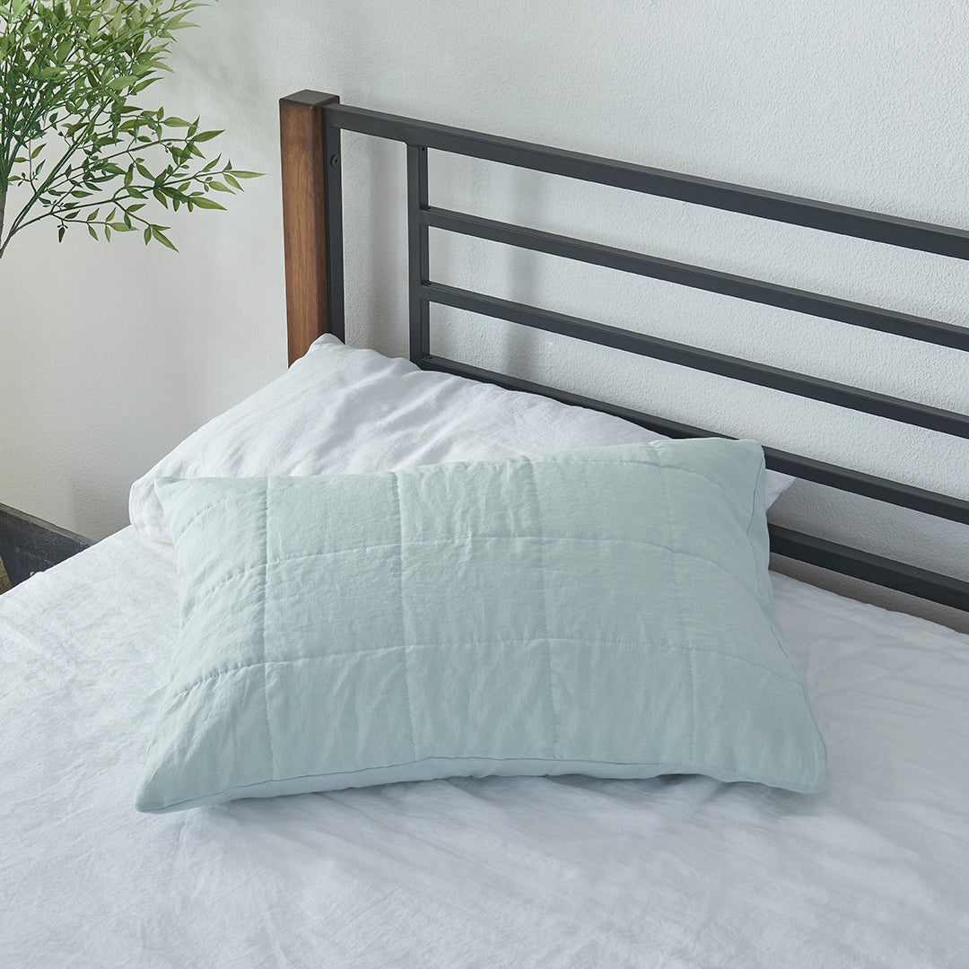 A pale blue 100% linen quilted pillowcase on a bed