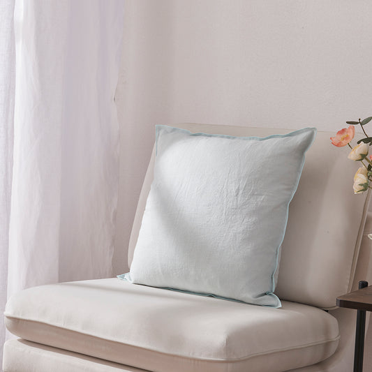 Side angle of a pale blue 100% linen edge embroidery cushion on an accent chair