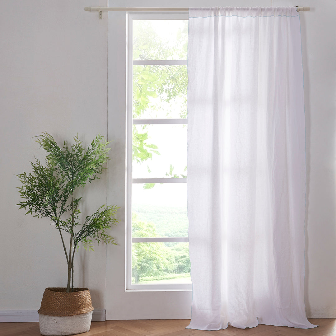 A 100% linen curtain with pale blue embroidered edges hanging over a window