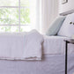 Side angle of a linen duvet cover with pale blue embroidered edges draped over a bed