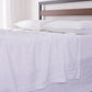 Detailed side angle of 100% linen flat sheet with pale blue colored edge embroidery laid over a bed