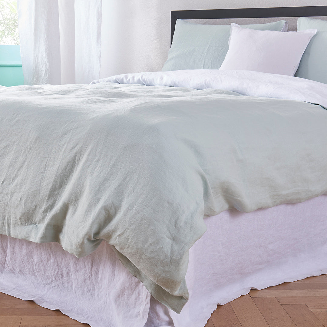 Corner bottom angle of 100% linen two tone duvet cover in pale blue and white draped over a bed