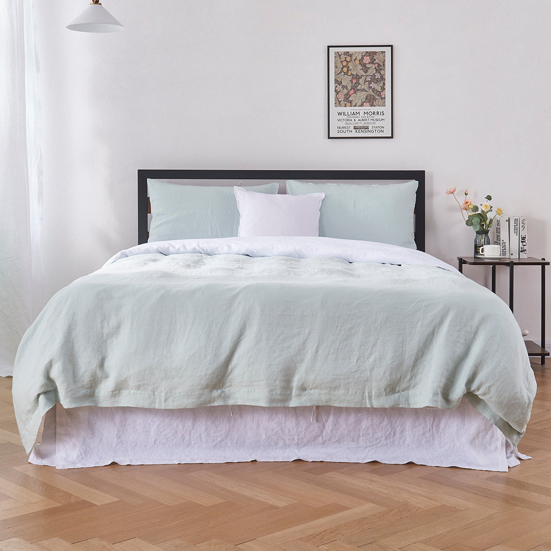 Bottom angle of 100% linen two tone duvet cover in pale blue and white draped over a bed