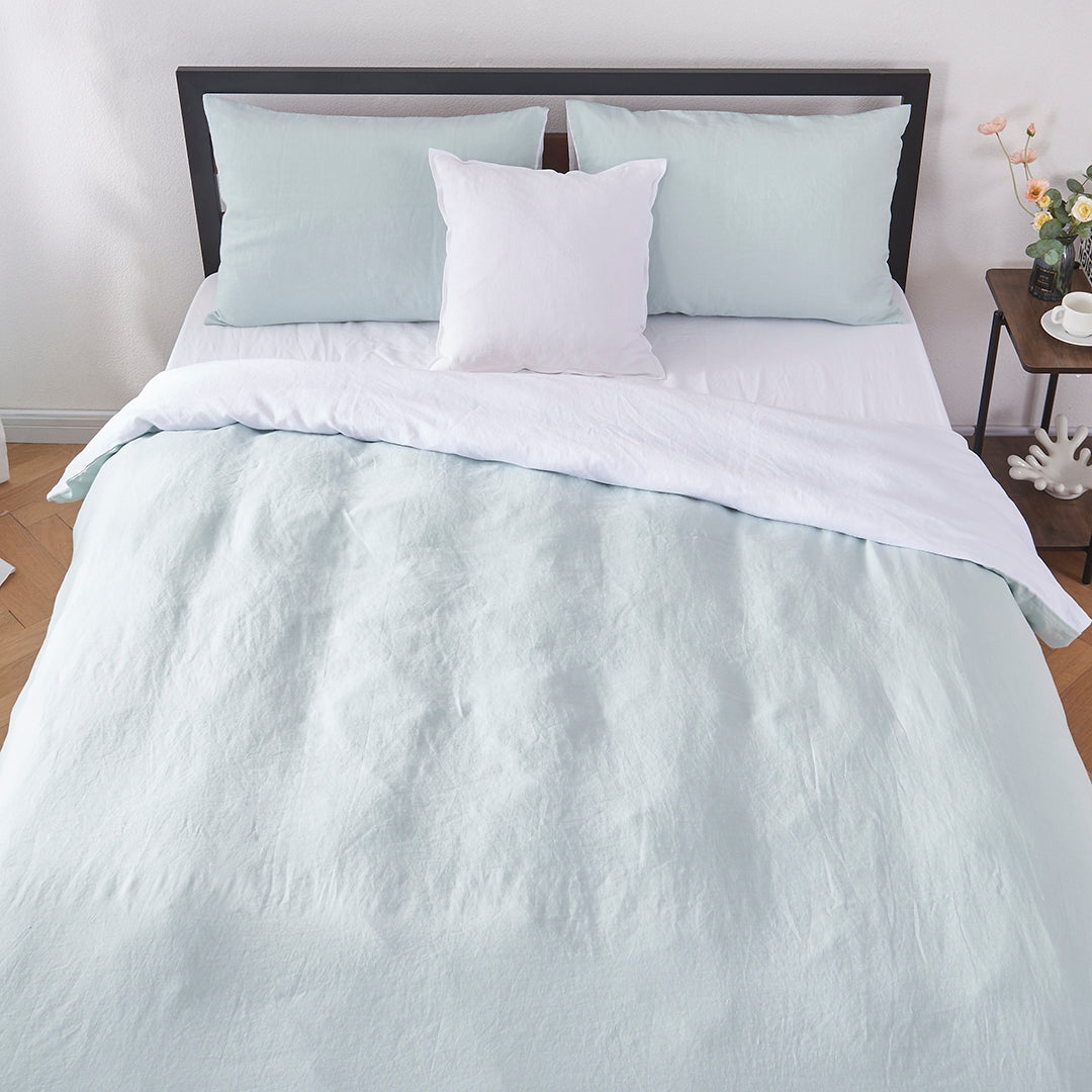 Top angle of 100% linen two tone duvet cover in pale blue and white draped over a bed