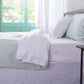 Side angle of 100% linen two tone duvet cover in pale blue and white draped over a bed