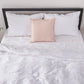 Top angle of a linen duvet cover with peach embroidered edges draped over a bed