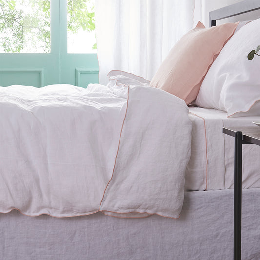 Side angle of a linen duvet cover with peach embroidered edges draped over a bed