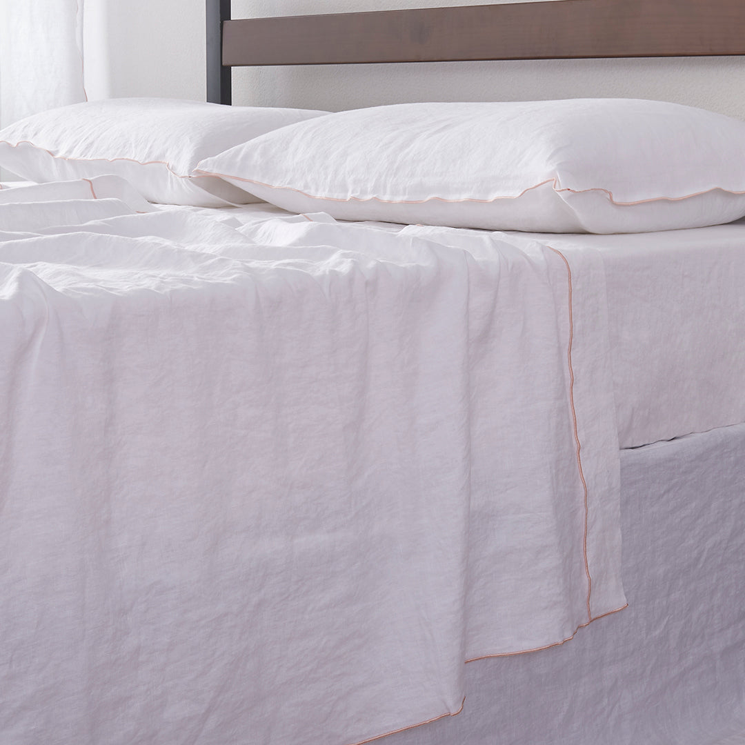 Detailed side angle of 100% linen flat sheet with peach colored edge embroidery laid over a bed