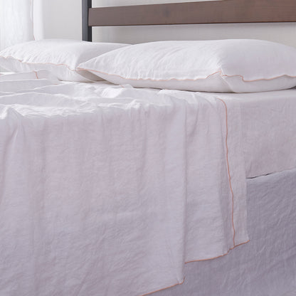 Detailed side angle of 100% linen flat sheet with peach colored edge embroidery laid over a bed