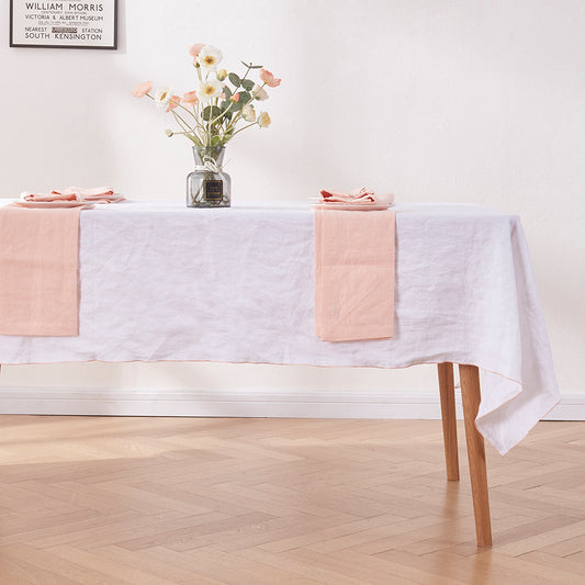 Close-up angle of peach edge embroidered linen tablecloth draped over a wooden table