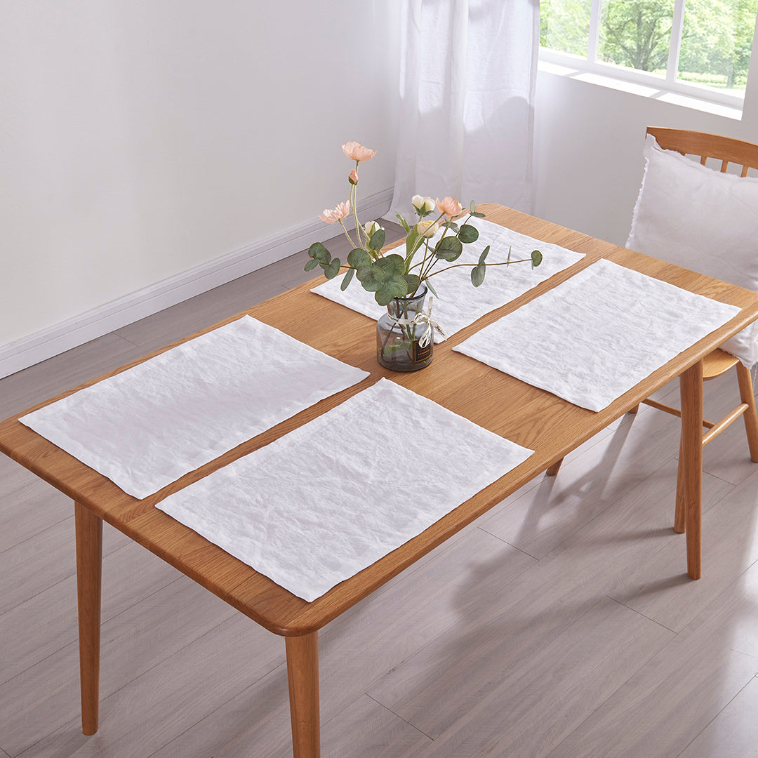 Optic white 100% linen placemats set on a wooden dining table with flower vase
