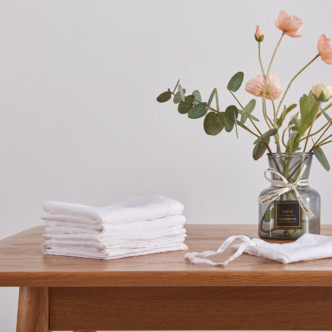 Optic white 100% linen placemats folded on a wooden dining table with flower vase