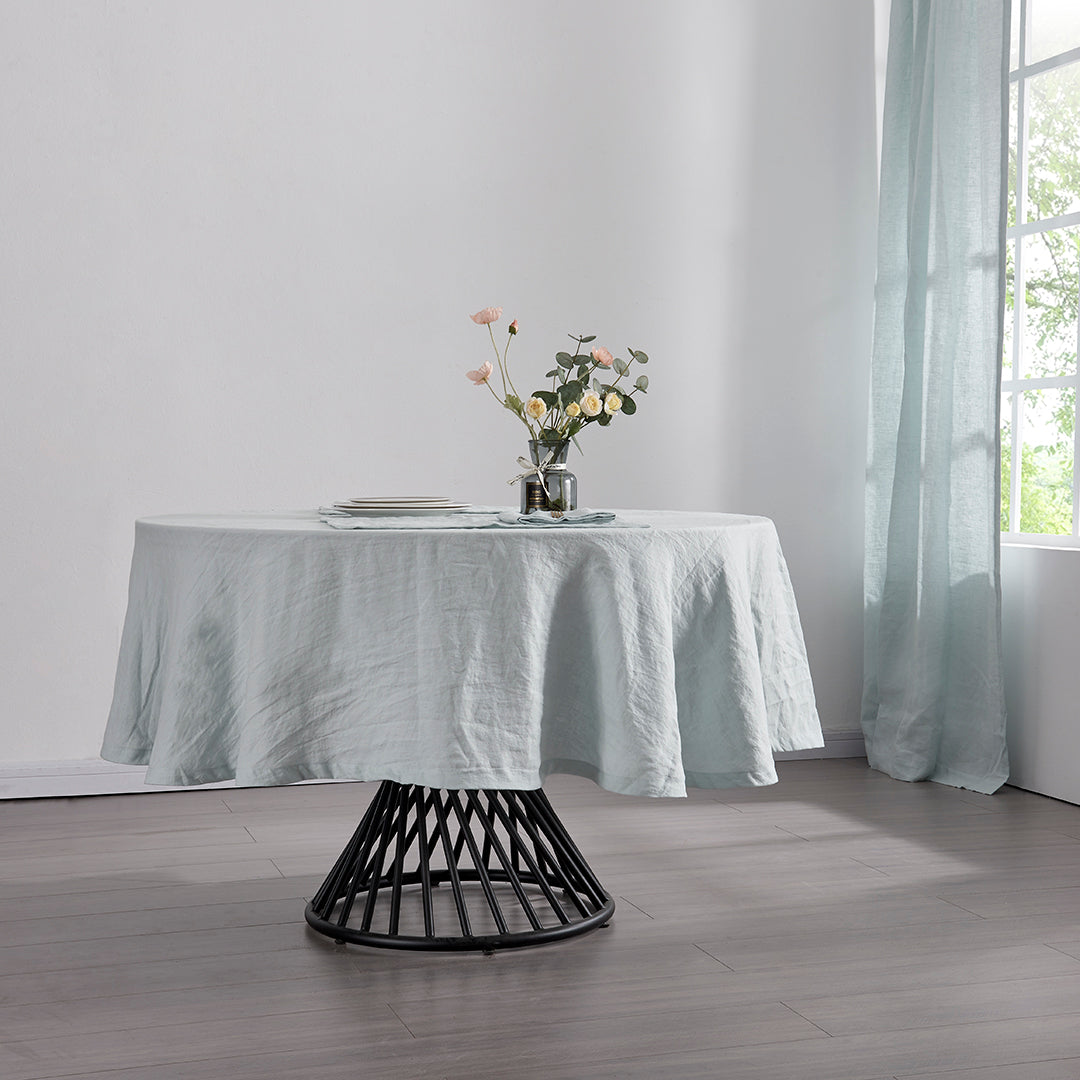 A 100% linen round tablecloth in pale blue draped over a round table