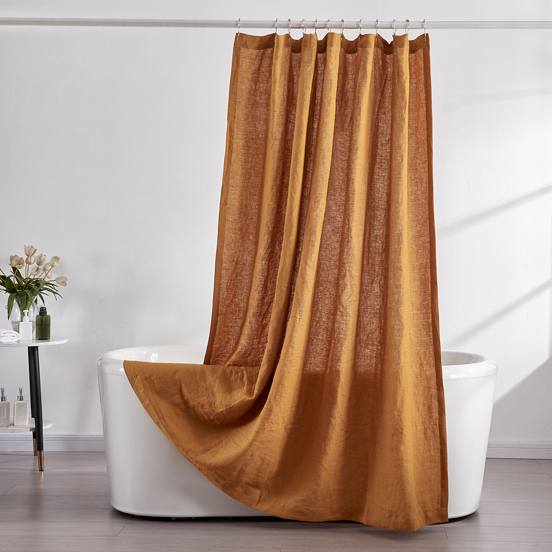 A 100% linen shower curtain in mustard draped over a ceramic bathtub