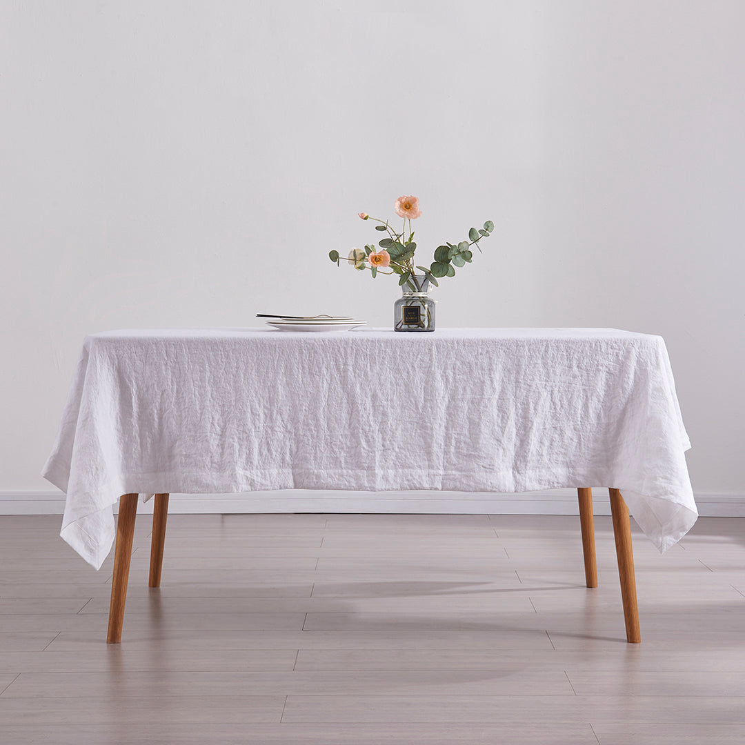 Optic white linen tablecloth draped over a wooden dining table