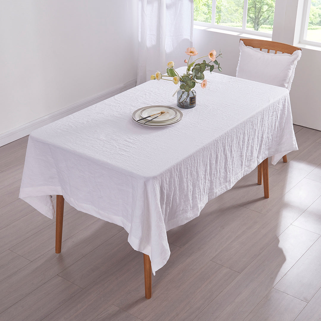 Top angle optic white 100% linen tablecloth draped over a wooden dining table