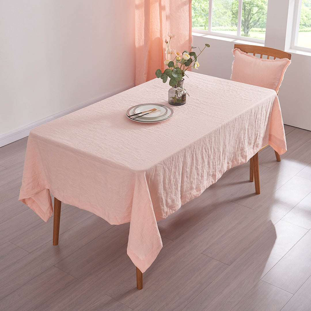 Top angle peach 100% linen tablecloth draped over a wooden table with flower vase
