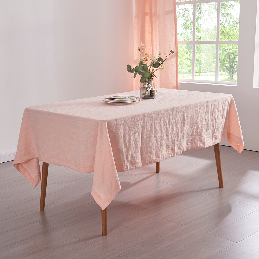 Corner angle peach 100% linen tablecloth draped over a wooden table with flower vase