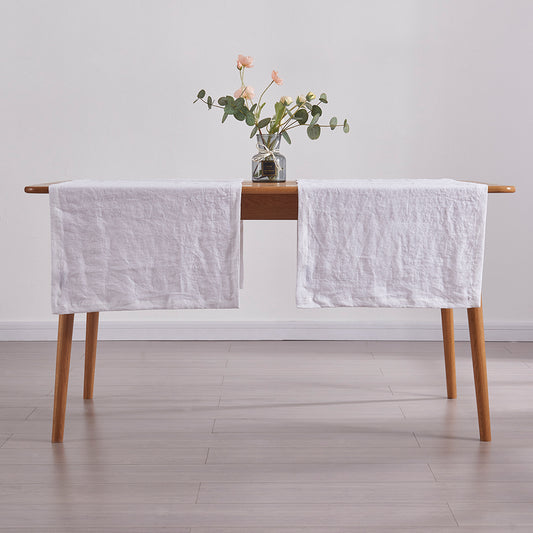 Optic white 100% linen table runners draped over a wooden dining table with flower vase