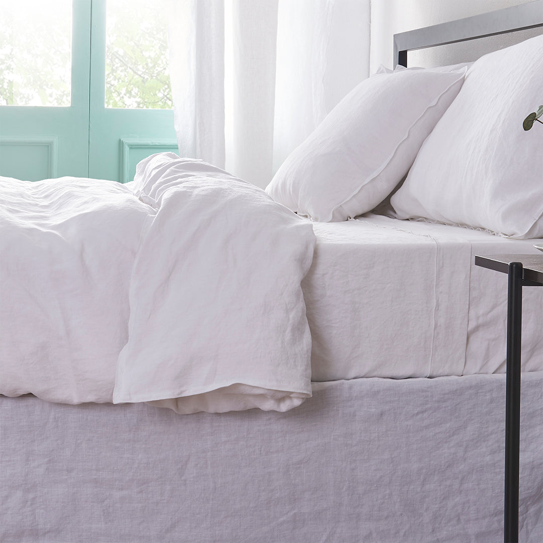 Side angle of a linen duvet cover with white embroidered edges draped over a bed