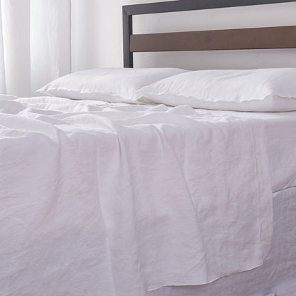 Detailed side angle of 100% linen flat sheet with white colored edge embroidery laid over a bed