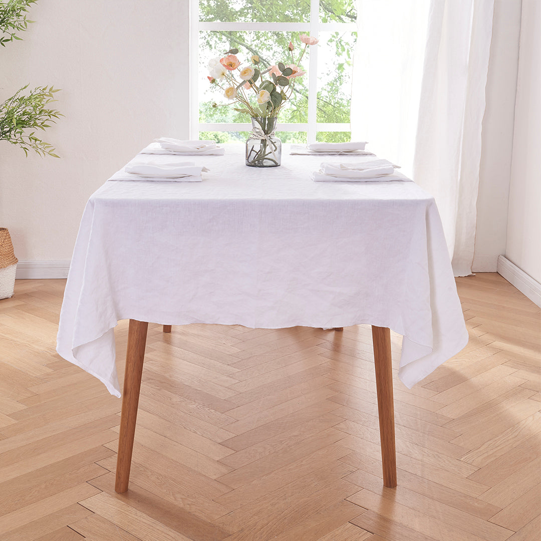 Side angle of white edge embroidered linen tablecloth draped over a wooden table