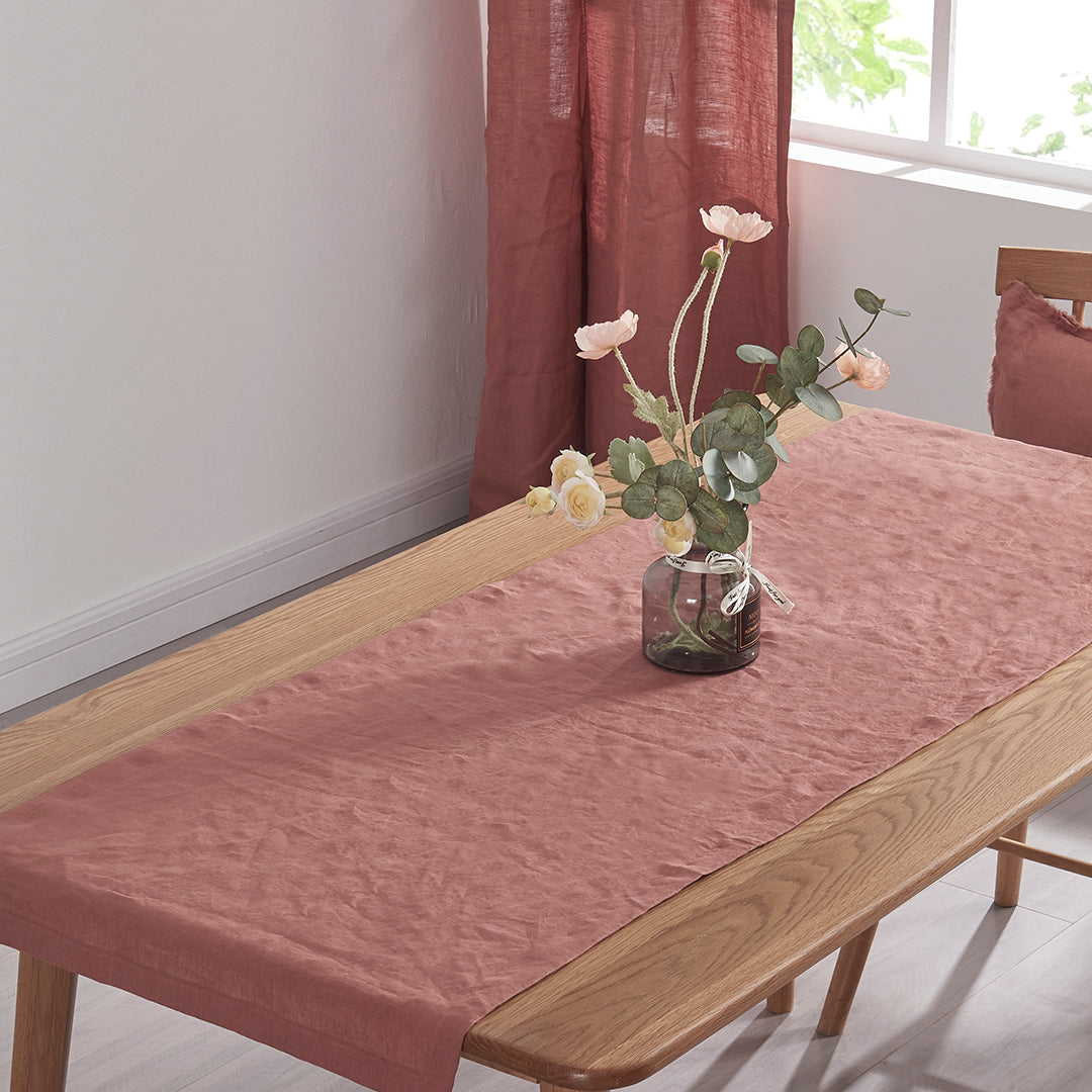 Rust red table runner made from 100% linen draped over a wooden table with flower vase